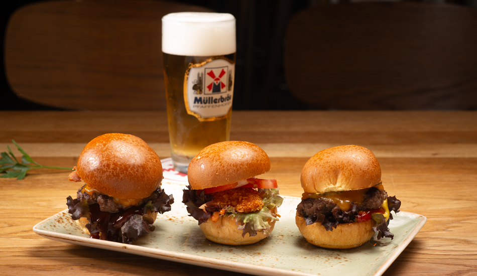 Drei kleine Miniburger mit verschienen Geschmacksrichtgungen, dahinter das Müller Helle Bier